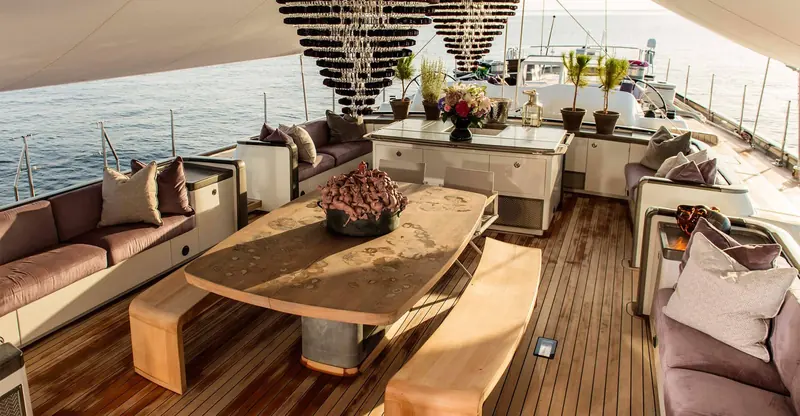 Pink Gin VI's aft deck as delivered in 2017, laid out for dining under sail with a jewel-toned palette and a live-edge table, the studio's original brief for her first owner.