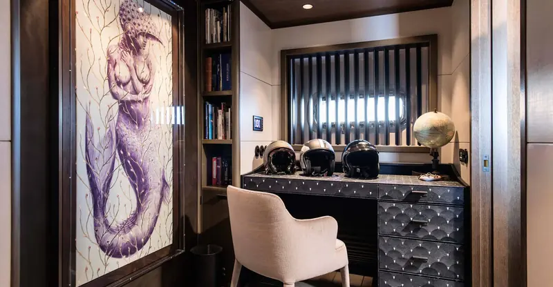 A study aboard Pink Gin VI in her original interior, with a commissioned mermaid painting and a run of racing helmets on the desk, the kind of one-off, owner-specific detail Design Unlimited builds into a custom brief.