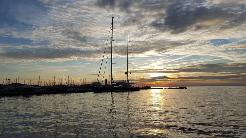 Mondango's twin masts against a Trieste sunset, moored at the same call in August 2019. The ketch rig and low, powerful sheerline are Dubois signatures across the studio's large sailing yachts.