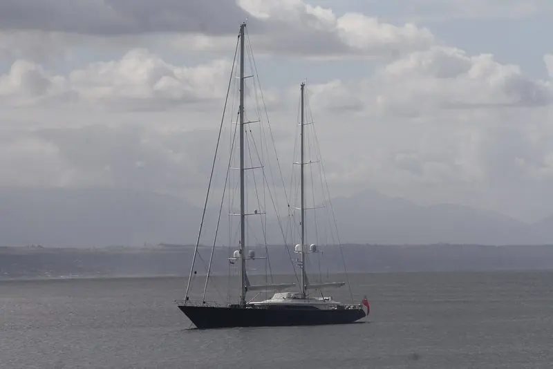 Fidelis sits to her anchor under low cloud with hills fading behind her.