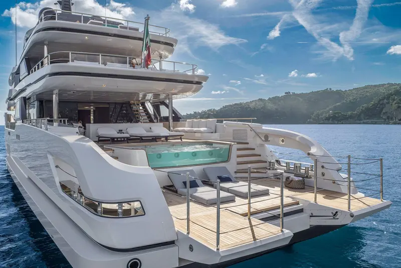 The Custom Line Navetta 50's transformable stern at anchor off a wooded headland on the Italian Riviera, sunpads folded out where Salvetti's exterior meets the water.