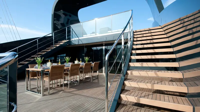 A YachtPlus Signature Series yacht's aft staircase and dining deck, glazed and chrome-railed over the dark grey hull Foster and Partners specified for the class.