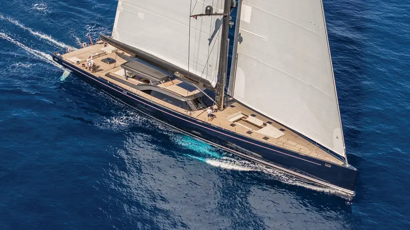 Atomic seen directly overhead, her teak deck laid out between two towering masts under a full press of sail.