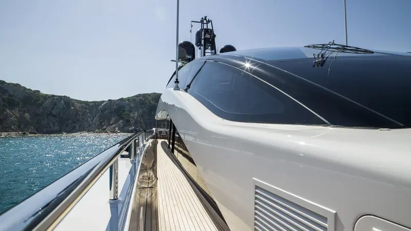 The side deck of Irisha, teak running forward under the curved glass panels that wrap her superstructure.