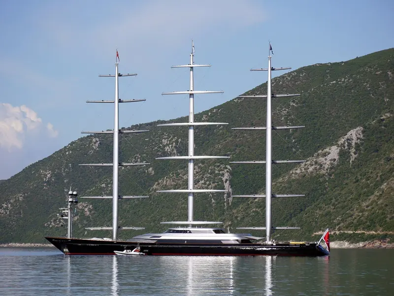 Maltese Falcon reaching along a mountainous coastline, the fifteen square sails of her three rotating masts fully set.
