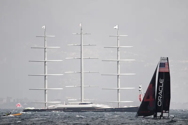 Maltese Falcon sailing in company with an America's Cup catamaran, a size comparison that shows how tall her DynaRig masts stand above the water.