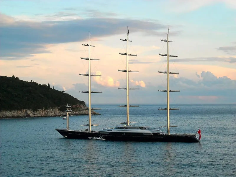 Maltese Falcon at anchor at dusk, masts bare, off a headland.