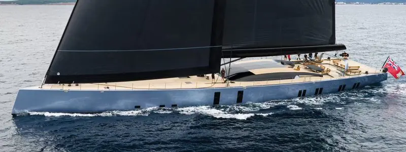 Crew work the deck of a sloop rigged sailing yacht making way under dark sails.