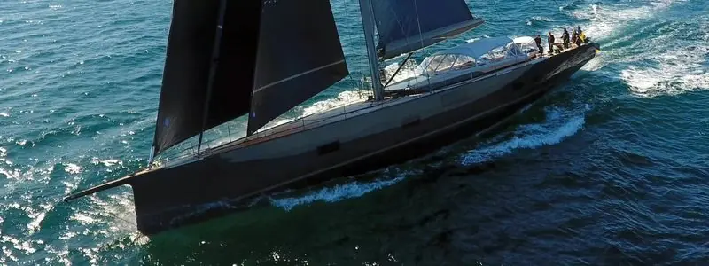 Heeling into a swell, a large sailing yacht throws white water down its lee side.