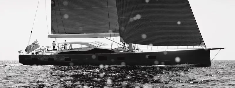 In black and white, a sailing yacht carries full sail with two crew standing aft.