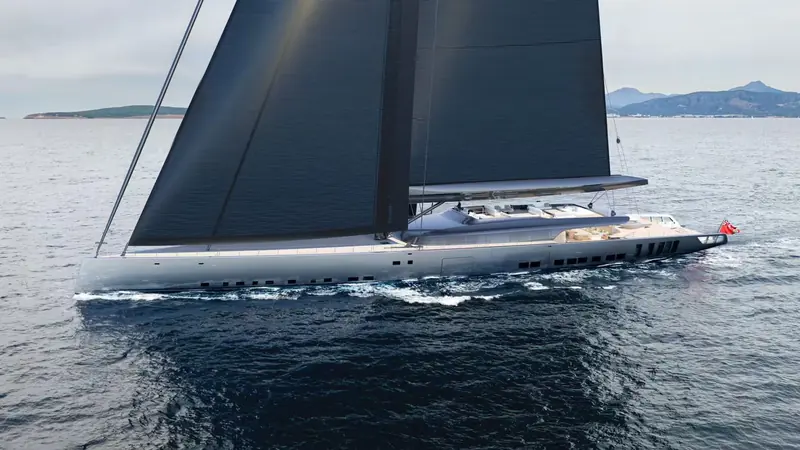 A black-sailed sloop heels under full canvas off a Mediterranean coastline, its silver hull cutting a clean wake.