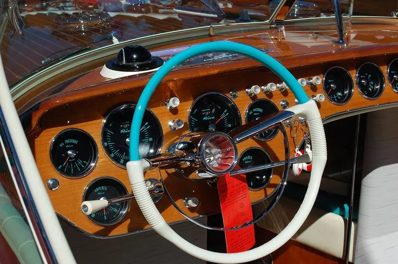 Turquoise wheel rim and black faced gauges fill the dashboard of a Riva Super Aquarama.