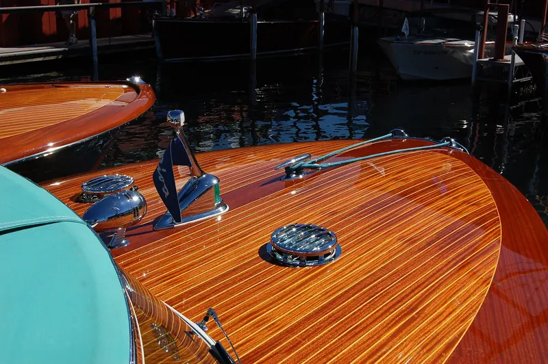 Sunlight rakes across the varnished foredeck, the fitted chrome cleats and hatch rings standing proud of the mahogany planking.
