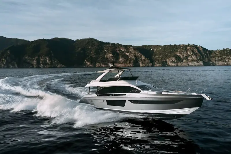 An Azimut Fly 68 at speed off a wooded headland, throwing the wide, aerated wake typical of the planing hull naval architecture built for this range.