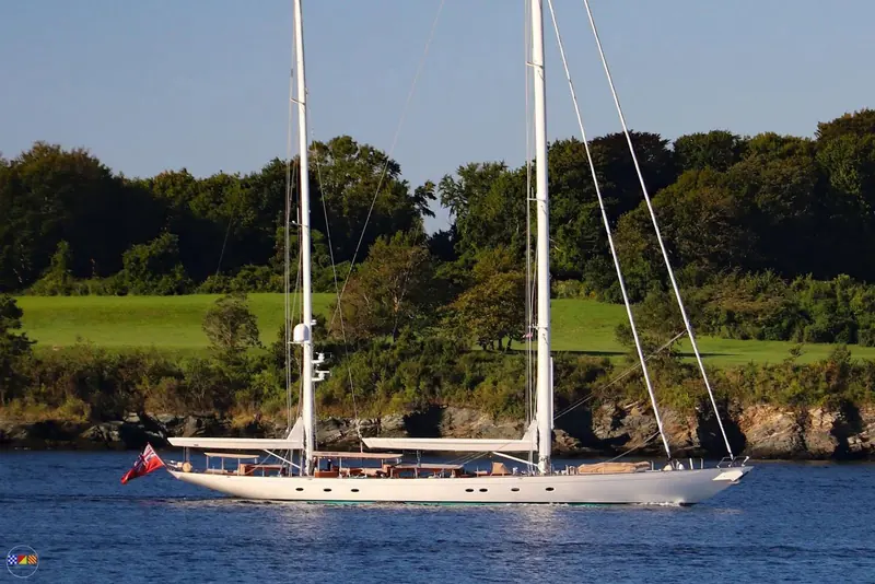 Meraki motoring past a wooded shoreline, sails furled, showing the full length of Hoek Design's hull and Rhoades Young's deck saloon glazing.