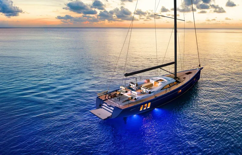 A Humphreys-designed Oyster riding at anchor at sunset, her underwater lighting on and mainsail still hoisted.