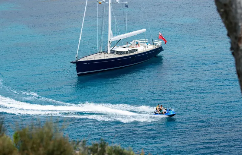 An Oyster anchored in a Mediterranean cove, red ensign flying, while her tender buzzes past under jet ski power.