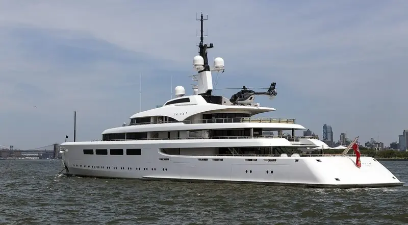 Vava II crosses New York Harbor with a helicopter secured aft and the Brooklyn Bridge behind.