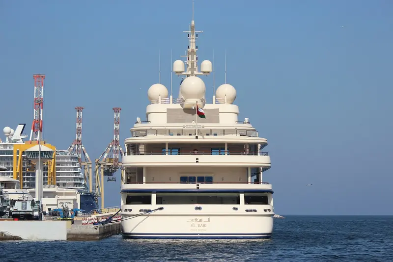 Al Said dockside at Mutrah Harbour, dwarfing the cranes and cruise terminal behind her - RWD's interior work on the 2007 rebuild is rarely photographed from this distance.