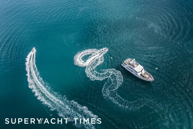 A tender carves a wake beside Marama at anchor, launched from her stern garage.