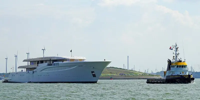The tug Dutch Pioneer walks an unpainted yacht hull down the Nieuwe Waterweg.