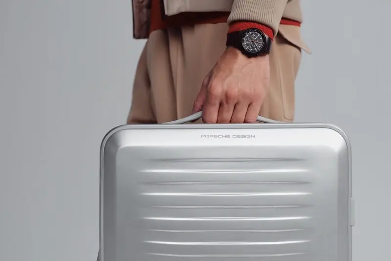 A traveller carries an aluminium case with a chronograph on the wrist above the handle.