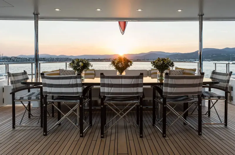 Brigadoon's aft deck dining table at dusk, laid for the kind of al fresco evening a residentially-trained studio designs around.