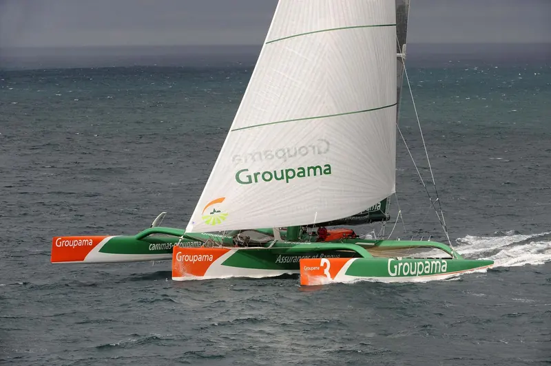 Groupama 3, Franck Cammas's 31.5m VPLP trimaran, bow-on under sail; she won the Jules Verne Trophy and the Route du Rhum in the same year, 2010, before a later career as Banque Populaire VII.