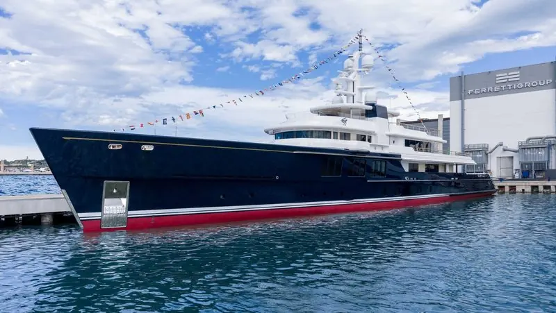 Signal flags run the length of a dark hulled motor yacht at a shipyard quay.