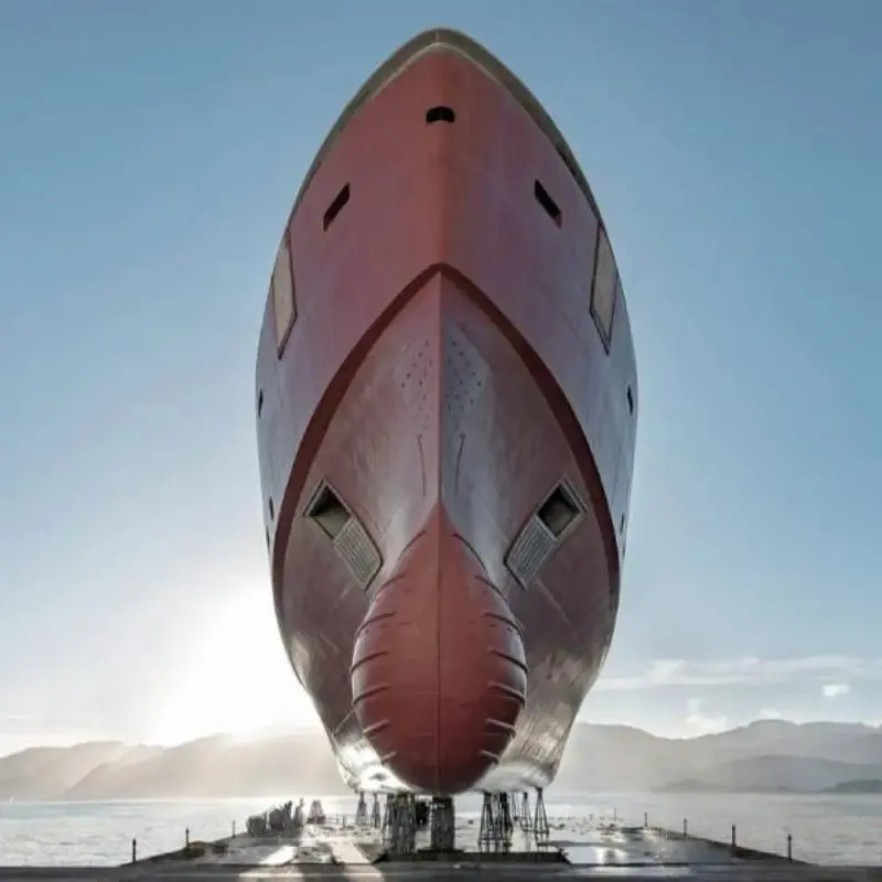 A freshly painted superyacht hull towers bow-on over the slipway in low sunlight ahead of a launch.