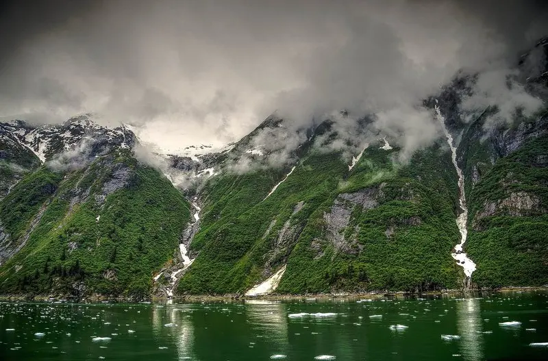 Cloud sits low on the walls of Tracy Arm, with snowmelt streaking the green slopes and brash ice scattered across the water.