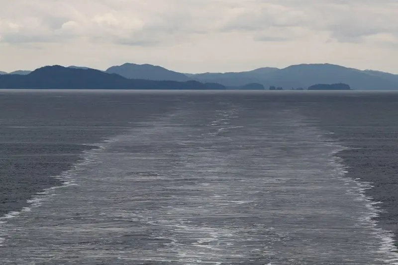 Wake runs back toward the low headlands south of Prince Rupert, the passage opening out under a flat sky.