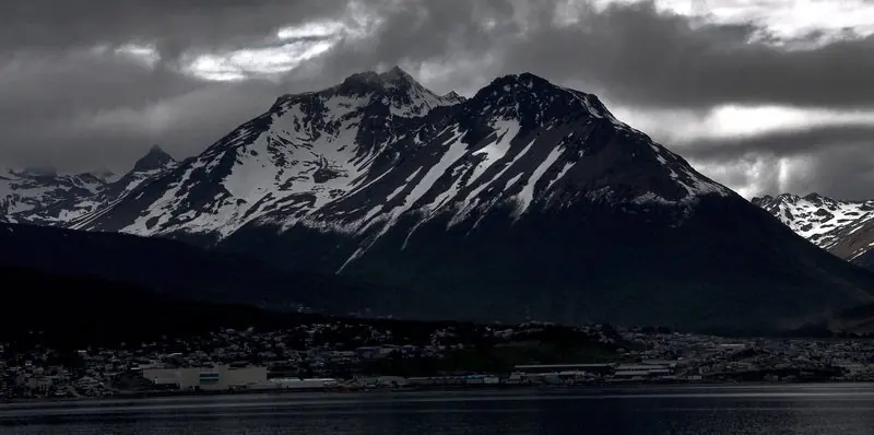 Snow streaked peaks stand over the town at the top of the channel, the harbour front in shadow under heavy weather.