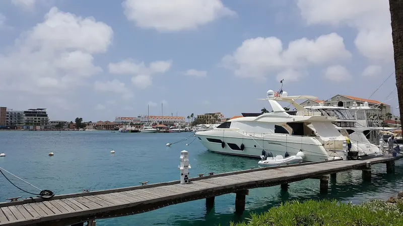 A motor yacht Med-moored at the downtown Oranjestad marina basin, resort towers and the old harbourfront behind it.