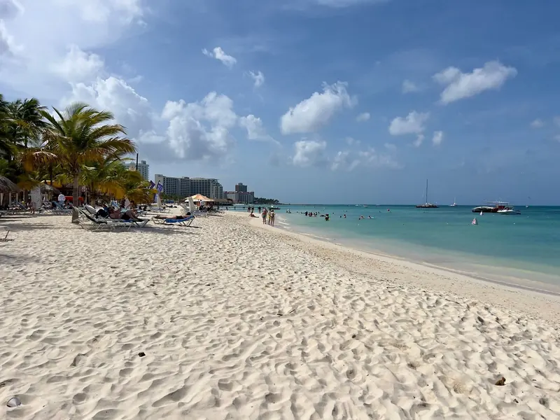 Palm Beach on Aruba's calm leeward coast, a sailing catamaran and small craft anchored offshore in flat turquoise water.