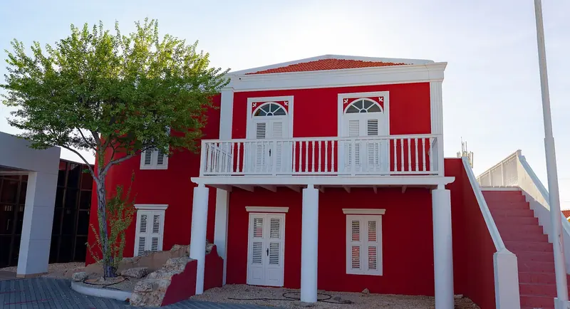 A restored red-and-white colonial building in downtown Oranjestad, the Dutch architecture that lines the harbourfront a yacht ties up beside.
