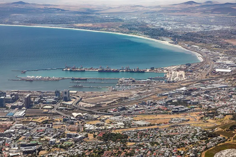 Table Bay's commercial port, cranes and naval vessels included, curls round the city with the Cape Flats stretching out behind.