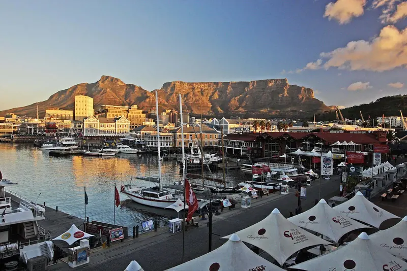 At the V&A Waterfront, yacht masts stand against Table Mountain in the evening light, with the marina restaurants beneath.