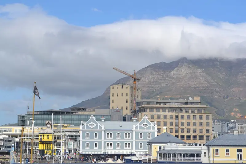 Cloud spills over Table Mountain above the Waterfront's gabled Victorian buildings and moored yacht masts.