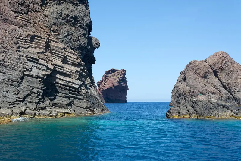 Rhyolite stacks at Punta Palazzu in the Scandola reserve, where the red rock drops sheer into water clear enough to read the bottom from the deck.