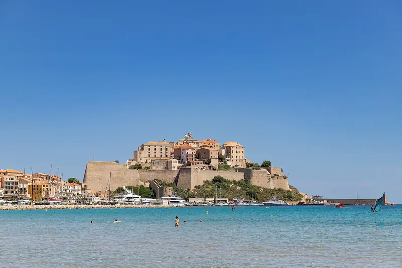 The Genoese citadel at Calvi stands over the bay with motor yachts on the marina quay below it and the mountains of the Balagne behind.