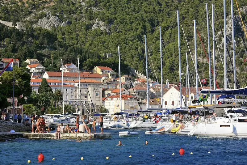 A Dalmatian town harbour in season, sailing boats rafted along the quay.
