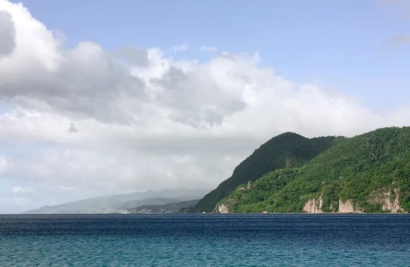 Soufriere Bay opens along Dominica's volcanic west coast, with Roseau visible in the distance under a heavy sky.