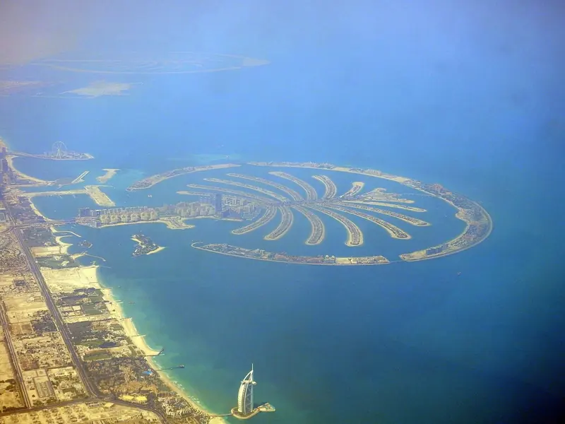 The Palm from the air at dusk, with the Gulf shallow and featureless beyond it and no natural anchorage within sixty miles.