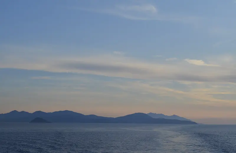 Elba at sunset from the water, Corsica's hills sometimes visible on a clear evening across the channel that separates the two islands.