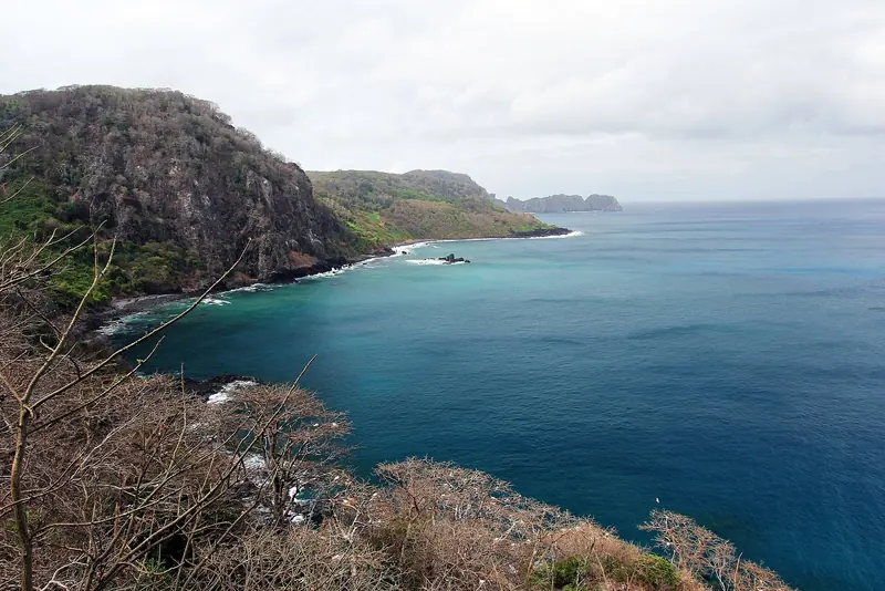 The cliff-lined coastline running toward Baia dos Golfinhos, the resting bay where resident spinner dolphins gather after their night of offshore feeding and where boats are barred from entering.