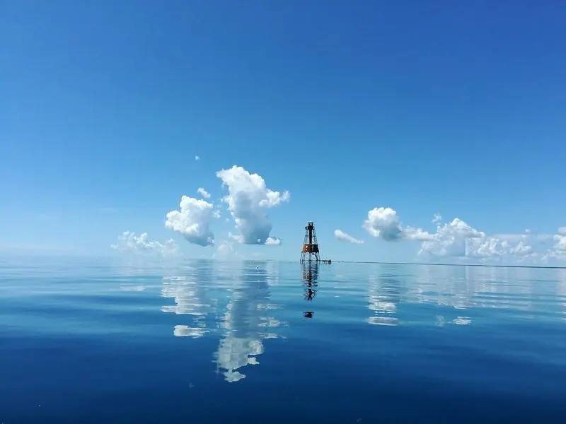 An iron screwpile lighthouse stands out on the reef in flat calm water, marking the shallow ground that runs the length of the Keys.