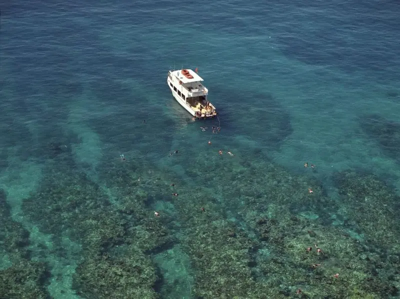 From above, a dive boat lies anchored over the reef off Key West with divers in the water and coral heads showing through the clear shallows.