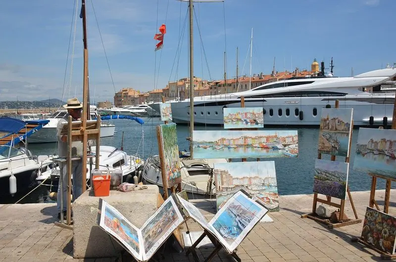 Painters work the quay at Saint-Tropez with a motor yacht berthed a few metres behind them.