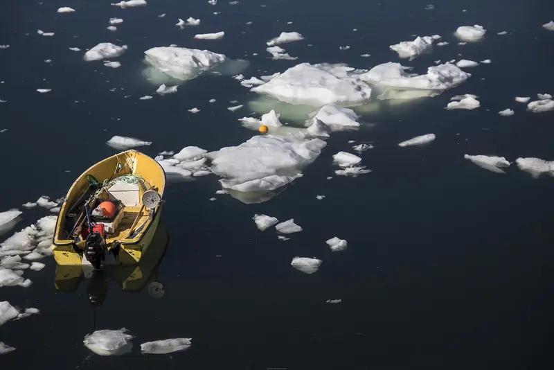 A small open boat picks a path between growlers in the ice near Ilulissat, the everyday scale problem any vessel faces working this coast.